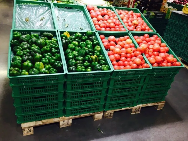 Green plastic crates in seasonal display rotation, holding fresh vegetables in a market.